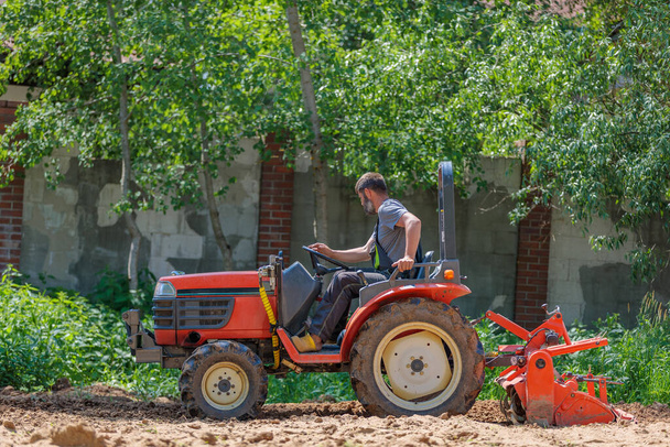 "A man on a mini-excavator levels a piece of land, loosens the soil." - Foto, afbeelding