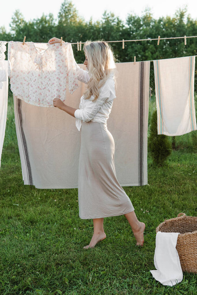 "Giornata di lavanderia. Una donna appende lenzuola e asciugamani ad un albero nel cortile di una casa di paese." - Foto, immagini