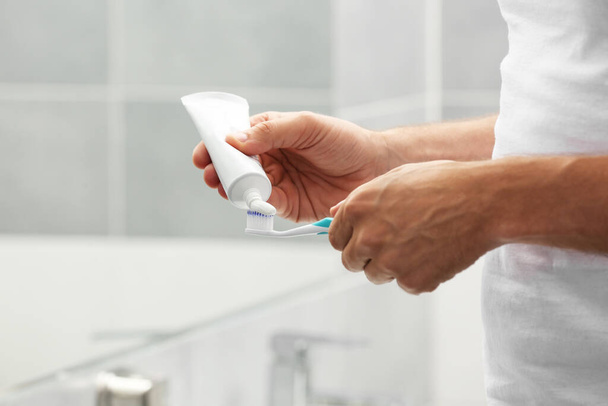Man applying toothpaste on brush in bathroom, closeup - Fotografie, Obrázek
