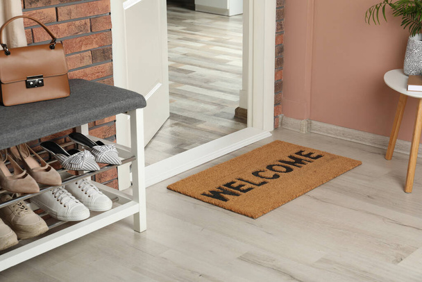 Doormat with word Welcome near shoe rack on white wooden floor in hall - Foto, Bild