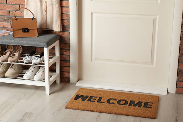 Doormat with word Welcome near shoe rack on white wooden floor in hall - Foto, Bild