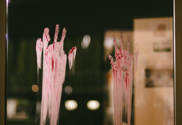 Portrait of bloody traces of adult hands on the glass of a window overlooking a blurred night landscape, side view close-up with selective focus. - Fotoğraf, Görsel