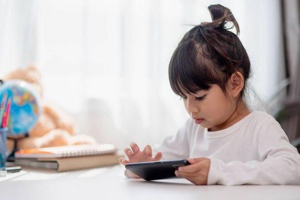 Aziatisch kind meisje hebben plezier thuis, met behulp van smartphone en lachen, het spelen van videospelletjes op een mobiele telefoon. kinderen en gadgets concept - Foto, afbeelding