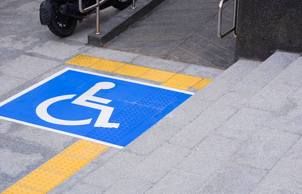 знак інвалідного візка з рампою та жовтою лінією тактильної тротуарної плитки на мармуровій поверхні тротуару різного рівня зі сходами у громадській зоні
 - Фото, зображення