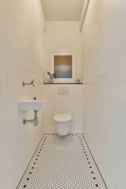 Interior of narrow restroom with sink and wall hung toilet with white walls - Photo, Image