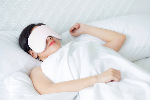 Krásná mladá Asiatka nosí krycí oko a spí na posteli s hlavou na polštáři pohodlí a štěstí v ložnici doma, dívka s relaxací a volný čas pro wellness, životní styl koncept. - Fotografie, Obrázek