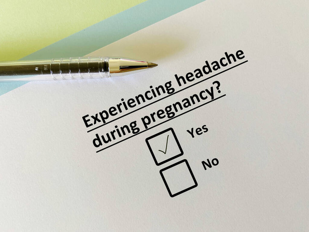Ένα άτομο απαντά σε ερώτηση σχετικά με την εγκυμοσύνη. Κατά τη διάρκεια της εγκυμοσύνης, βιώνει πονοκέφαλο. - Φωτογραφία, εικόνα