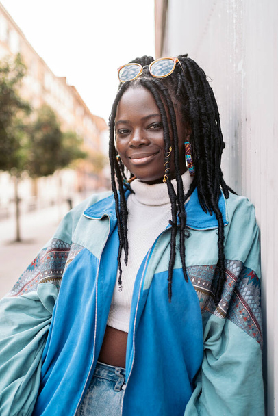 Happy and young african woman with cool braids smiling and looking at camera in the city. - Φωτογραφία, εικόνα