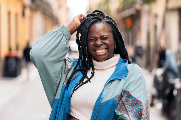 Happy young african woman with cool braids laughing and looking at camera in the city. - 写真・画像