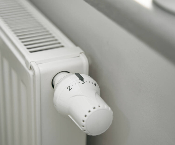 Nahaufnahme des Abschaltens des Thermostats an einem Heizkörper, um Energie zu sparen, weil die Heizkosten steigen. Konzept der Kosteneinsparung bei Kälte und Energiekrise. - Foto, Bild