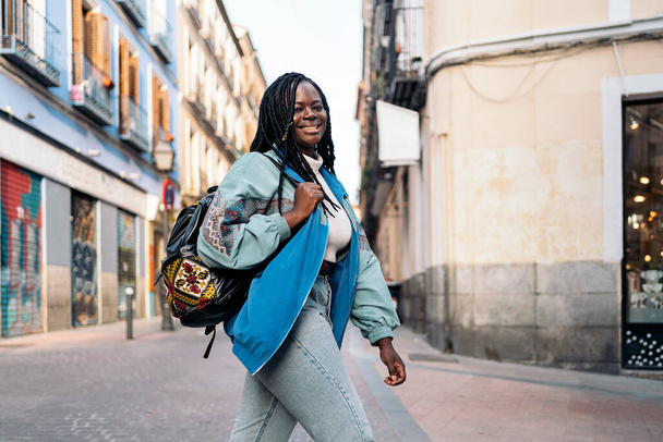 Sıradan giysileri olan mutlu Afrikalı kadın şehirde yürüyor ve kameraya bakıyor.. - Fotoğraf, Görsel