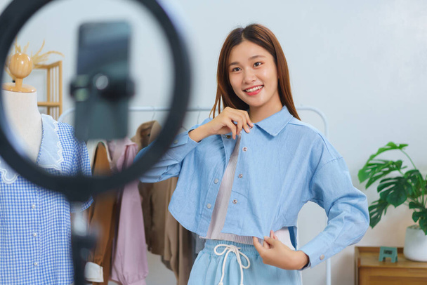 Online-Marketing-Konzept, junge asiatische Frauen probieren Hemd an und präsentieren Details im Streaming-Video. - Foto, Bild