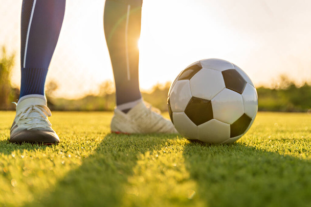 Спортсмен, стоящий с мячом на футбольном поле во время восхода солнца, футбольный мяч в сетке на фоне неба, движение мяча, популярные виды спорта на футбольном клубе. - Фото, изображение