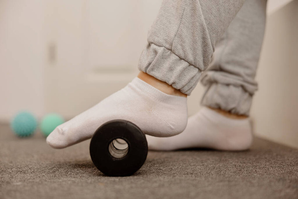 Woman doing flatfoot correction gymnastic exercise using massage roller. Myofascial relaxation of foot muscles. Hallux valgus. Pain. Identification of flat feet. Self care practices at home, health - Photo, Image