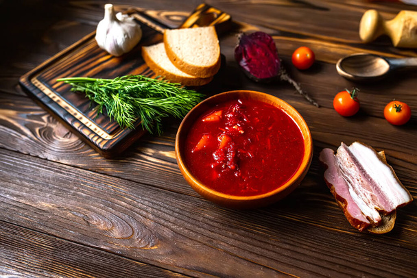 伝統的なウクライナのロシアのボルシチやボウルに赤いスープ.暗い木の背景で調理するための野菜のセットとボード - 写真・画像