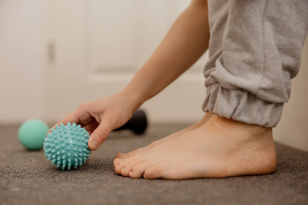 Woman doing flatfoot correction gymnastic exercise using massage ball. Myofascial relaxation of foot muscles. Hallux valgus. Pain. Identification of flat feet. Self care practices at home, healthcare - Photo, Image