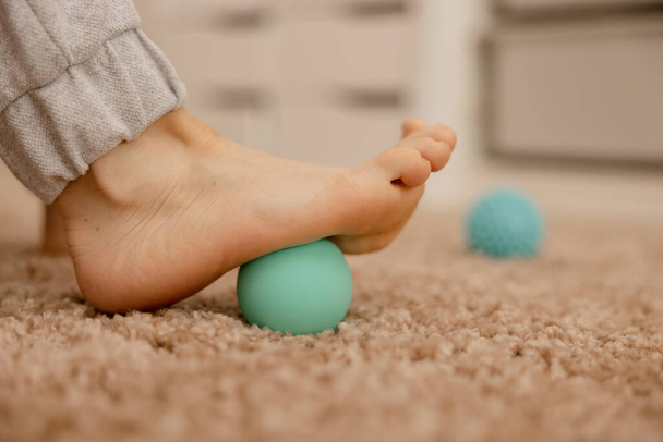 Woman doing flatfoot correction gymnastic exercise using massage ball. Myofascial relaxation of foot muscles. Hallux valgus. Pain. Identification of flat feet. Self care practices at home, healthcare - Photo, Image