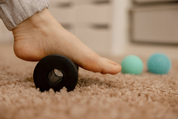 Woman doing flatfoot correction gymnastic exercise using massage roller. Myofascial relaxation of foot muscles. Hallux valgus. Pain. Identification of flat feet. Self care practices at home, health - Photo, Image