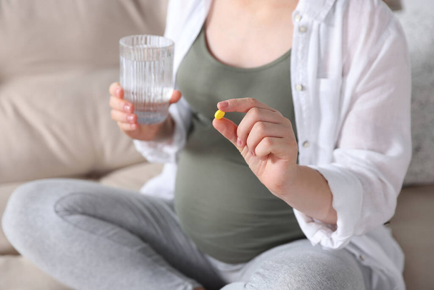 Pregnant woman holding pill and glass with water on sofa, closeup - Foto, Imagem