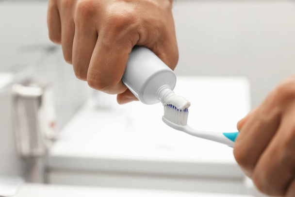 Man applying toothpaste on brush in bathroom, closeup - Zdjęcie, obraz