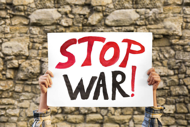 Woman holding poster with words Stop War against brick wall outdoors, closeup - Fotó, kép