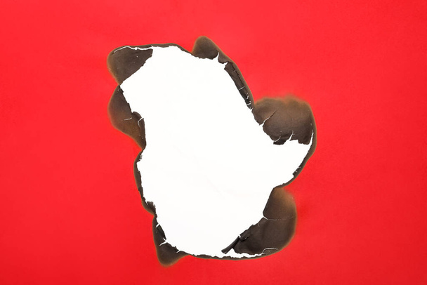 Burnt hole in red paper on white background, space for text - Fotó, kép