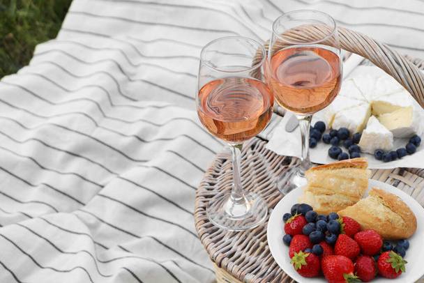 Glasses of delicious rose wine, food and basket on picnic blanket outdoors - Fotó, kép