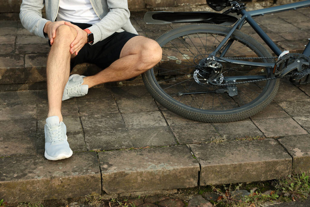 Man with injured knee on steps near bicycle outdoors, closeup - Photo, image