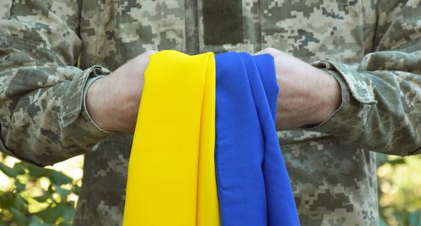 Украинский военный держит в руках национальный флаг как символ силы. Война на Украине. День казачества и защитника Украины. - Фото, изображение