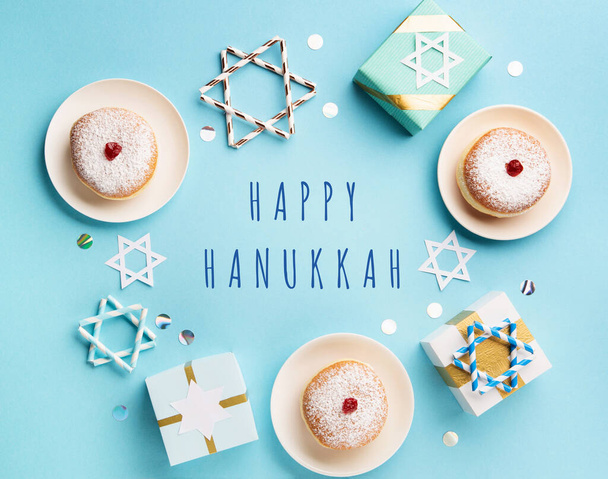 Hanukkah sweet doughnut sufganiyot with powdered sugar and fruit jam, gift boxes on blue paper background. Jewish holiday Hanukkah concept. Top view, copy space - 写真・画像