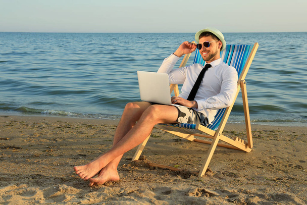 Happy man with laptop on deckchair near sea. Business trip - Zdjęcie, obraz