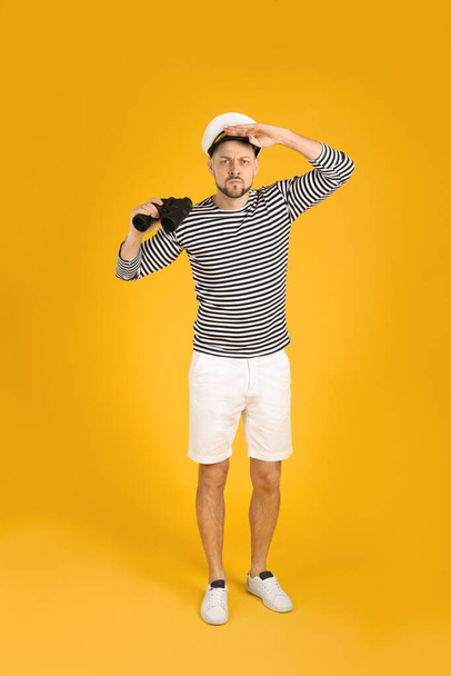 Serious sailor man with binoculars on yellow background - Photo, Image
