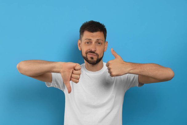 Man showing thumbs up and down on light blue background - Foto, Imagem