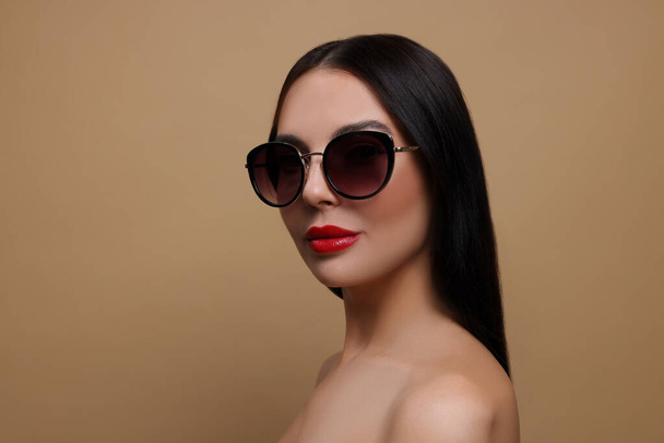 Attractive woman in fashionable sunglasses against beige background - Foto, Bild