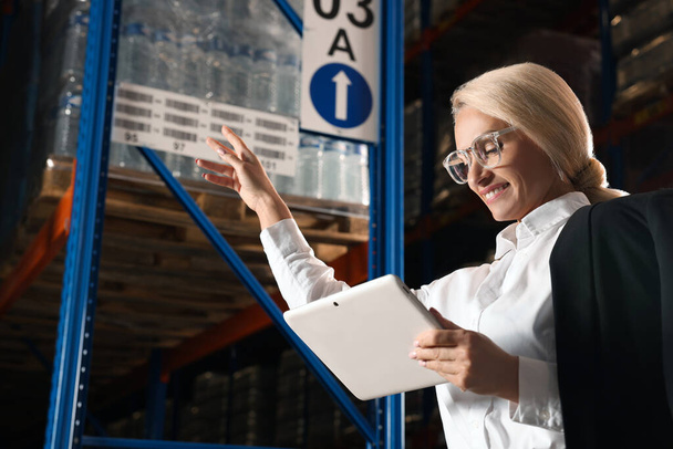 Happy manager holding modern tablet in warehouse with lots of products. Space for text - Foto, Imagem