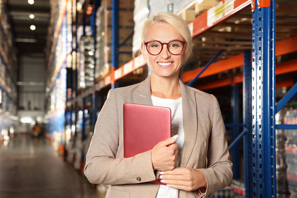 Happy manager holding modern tablet in warehouse with lots of products - Fotó, kép
