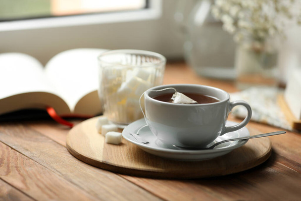 Tray with cup of freshly brewed tea and sugar cubes on wooden table, space for text - Fotó, kép