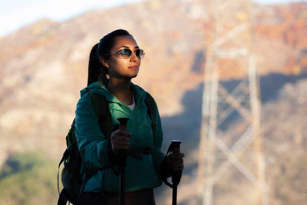 Hiker girl with hiking poles and backpack. Huge electricity transmission line tower in the background. - Φωτογραφία, εικόνα
