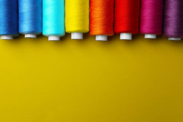 Set of different colorful sewing threads on yellow background, flat lay. Space for text - Foto, Bild