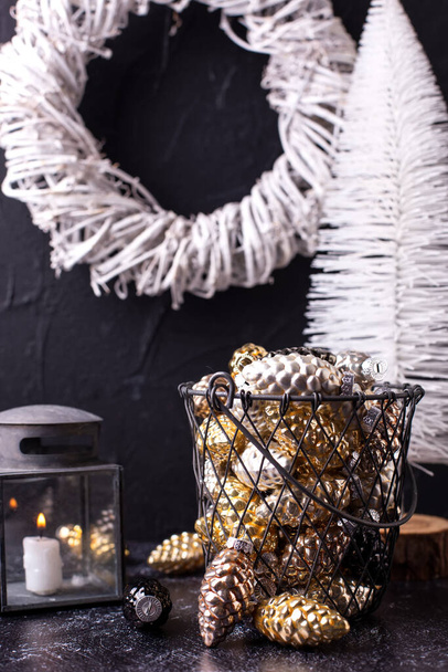 New Year decorations. Metallic bucket with decorative glass cones and white handmade wreath on black textured background. Scandinavian minimalistic style. Still life - Foto, imagen