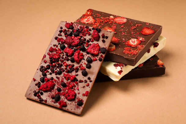 Different chocolate bars with freeze dried fruits on beige background - 写真・画像