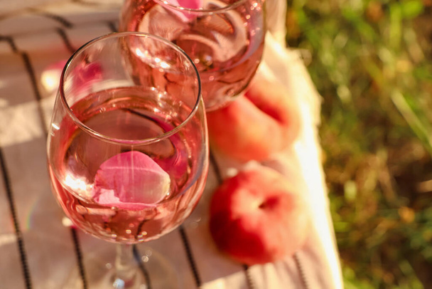 Glasses of delicious rose wine with petals and peaches on white picnic blanket outside. Space for text - Fotografie, Obrázek