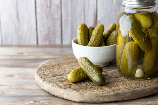 A jar of homemade dill pickles with a bowl full and pickles in front on a wooden board. - Photo, Image