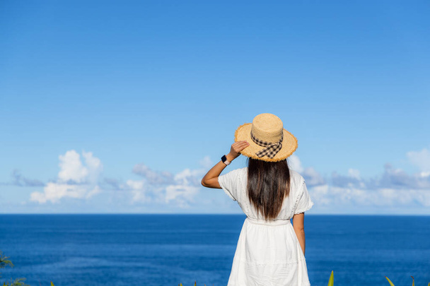 Toeristische vrouw met witte jurk en kijk naar de zee in de zomer - Foto, afbeelding
