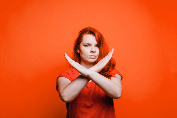 Jonge roodharige vrouw toont duimen naar beneden gebaar, heldere rode achtergrond - Foto, afbeelding