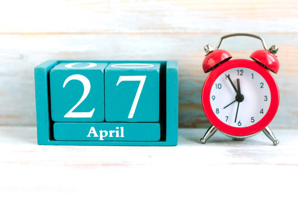 27 Nisan. Ay, tarih ve ahşap zemin üzerinde kırmızı alarm saati olan mavi küp takvimi - Fotoğraf, Görsel