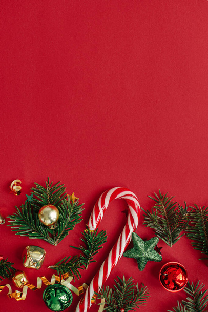 Moderno piso de Navidad. Elegantes adornos de Navidad, ramas de abeto, confeti y bastón de caramelo sobre fondo rojo. Plantilla de tarjeta de felicitación Seasons, espacio para texto. ¡Feliz Navidad! Vacaciones de invierno - Foto, imagen