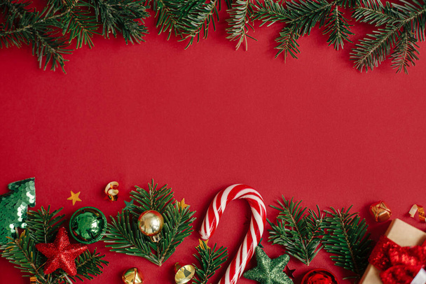 現代のクリスマスのフラットレイアウト。赤い背景にスタイリッシュなクリスマスの泡、モミの枝、コンフェッティとキャンディーの杖。季節グリーティングカードテンプレート、テキストのためのスペース。メリークリスマス！冬休み - 写真・画像