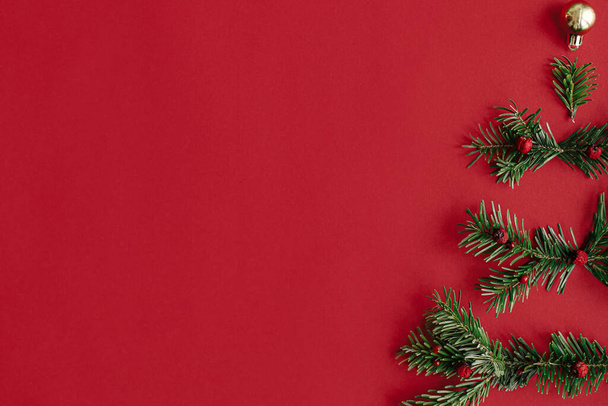 Boldog karácsonyt! Modern karácsonyfa, téli ünnepek koncepciója. Stílusos karácsonyfa fenyő ágakból, baubles, arany konfetti vörös háttérrel, ünnepi lapos fektetés. Kreatív ötlet. - Fotó, kép