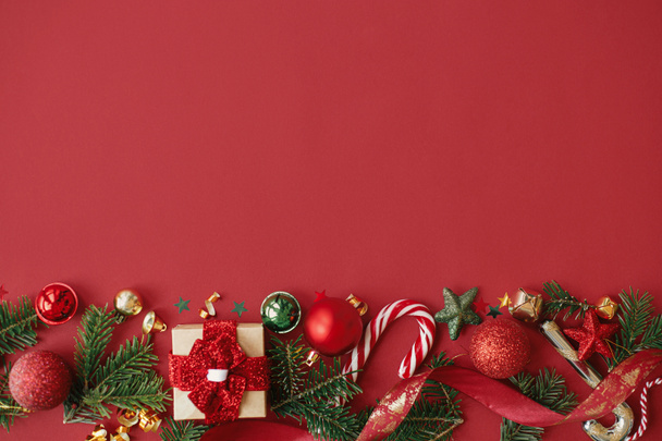 Modern karácsonyi lakás feküdt. Stílusos karácsonyi ajándék, baubles, fenyő ágak, konfetti és cukornád piros alapon. Boldog karácsonyt! Évszakok üdvözlő kártya sablon, hely a szövegnek. Téli ünnepek - Fotó, kép